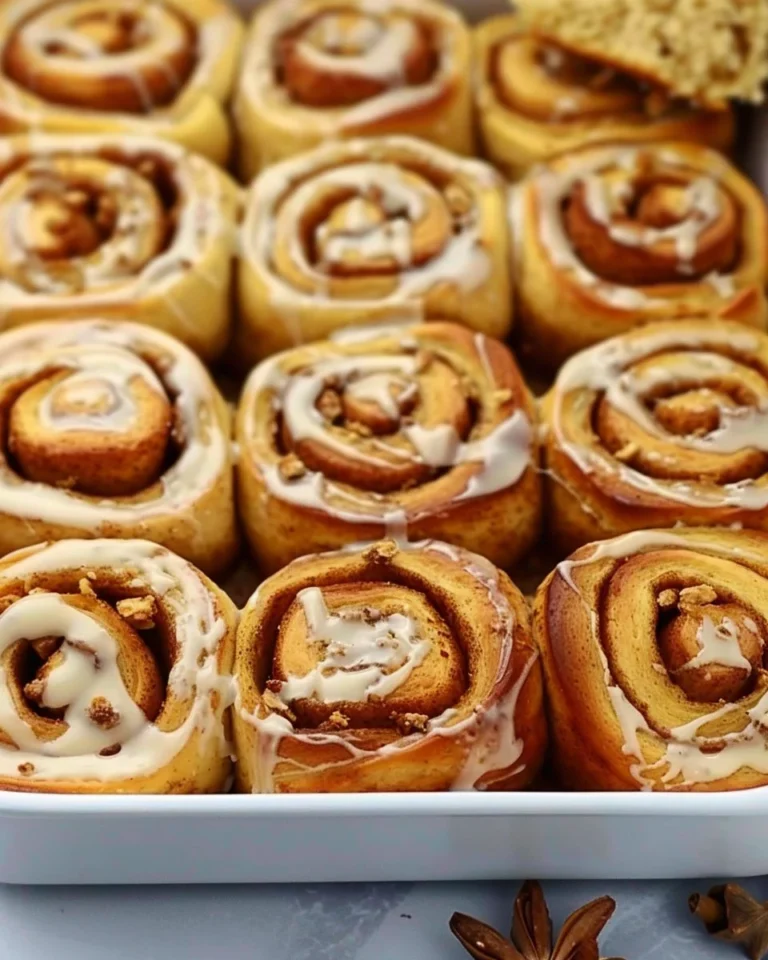 Sourdough pumpkin cinnamon rolls with maple cream cheese frosting on a plate.